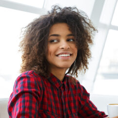 Portrait of pretty young african american woman wearing plaid shirt smiling and drinking coffee in cafe