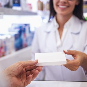 At the pharmacy. Beautiful young female pharmacist is offering a medication to a client while working at the cash desk